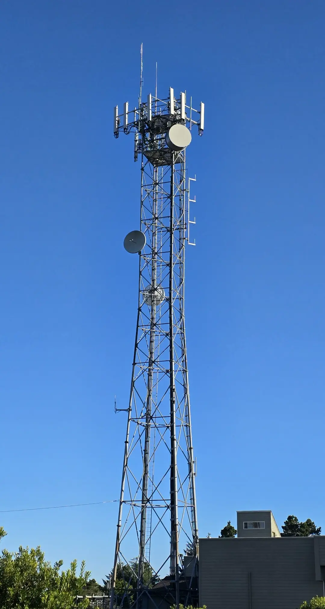 Lattice steel cell tower carrying antennas and microwave dishes against a blue sky