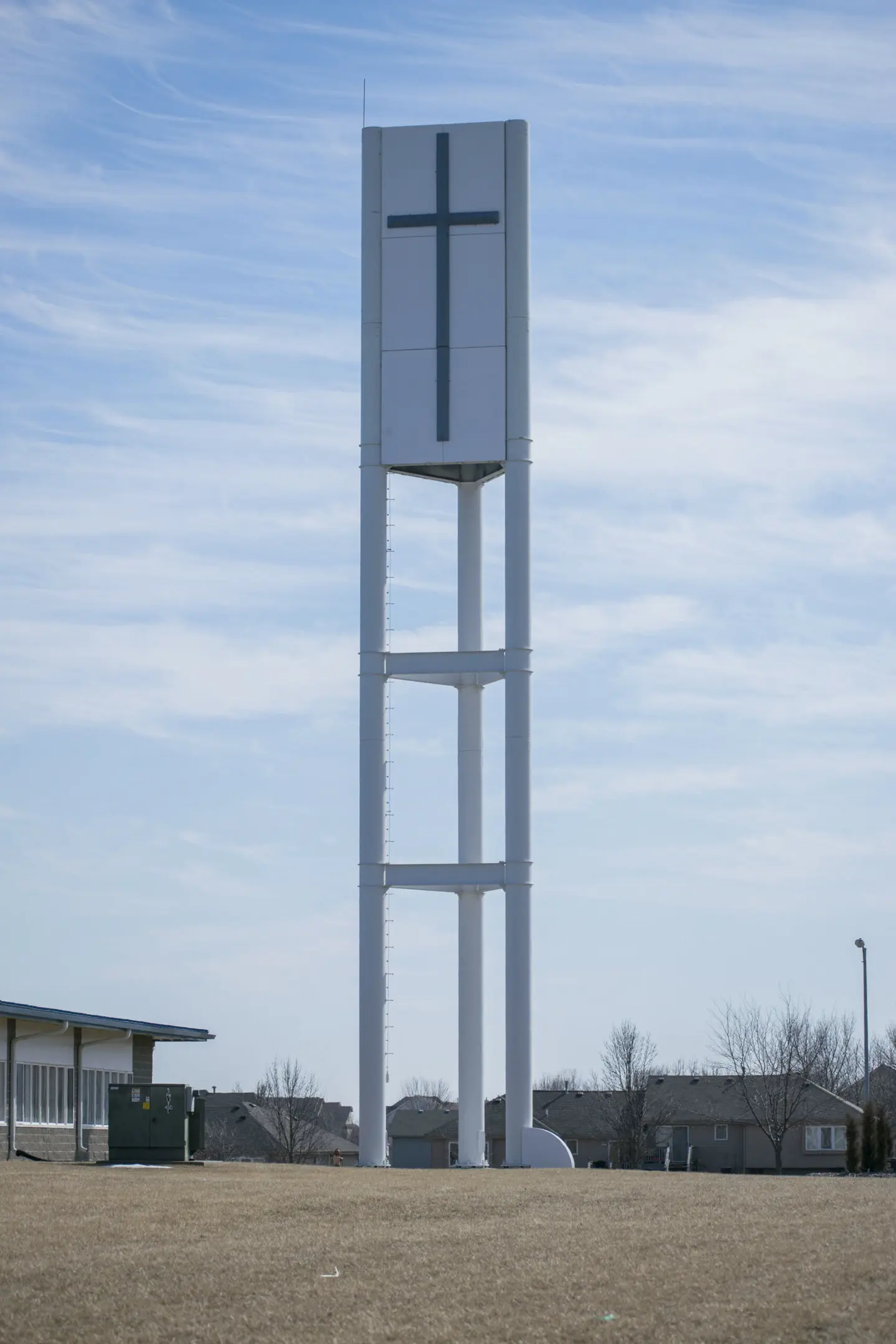 Tall steel bell-tower style cross structure standing on an open lawn