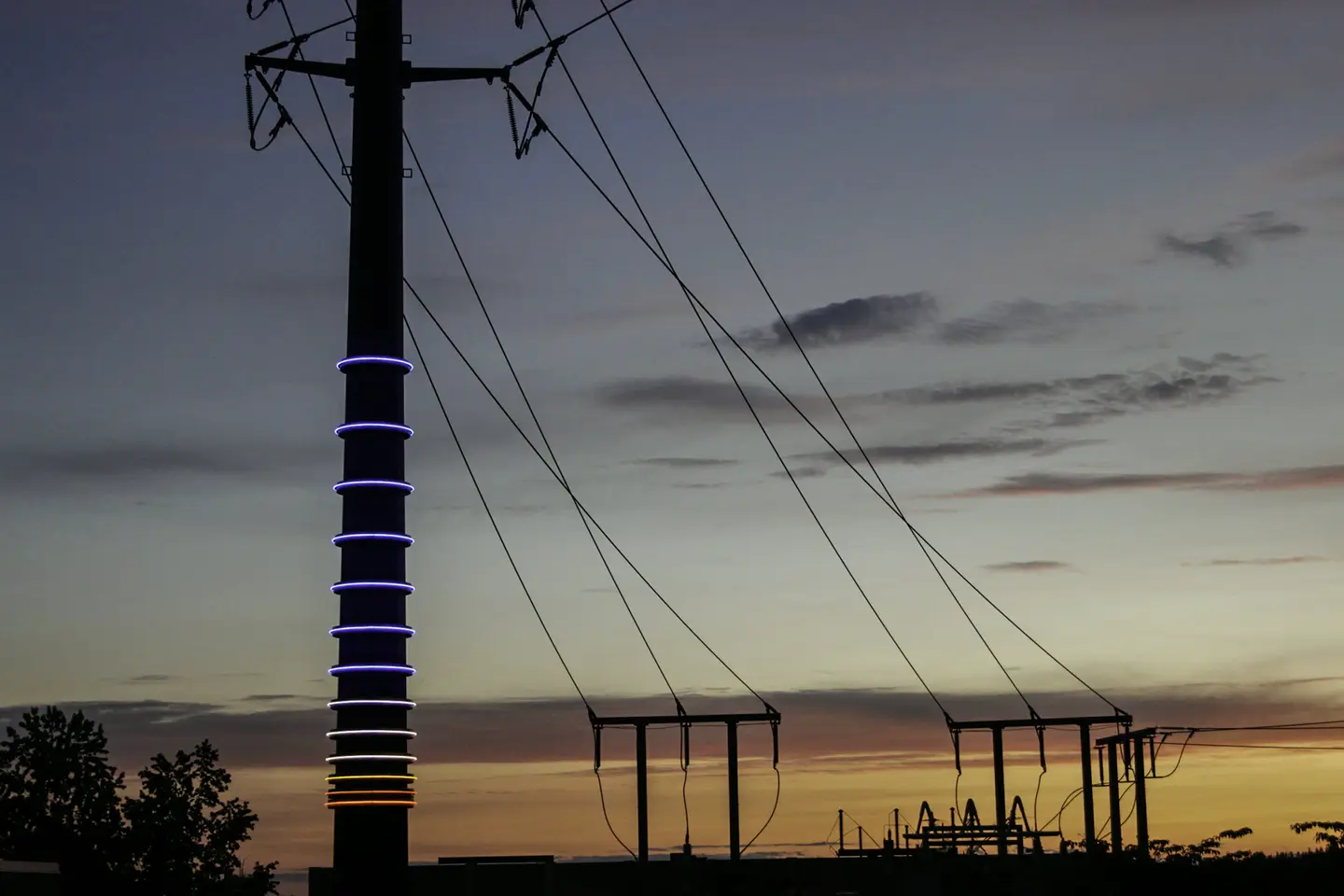 Transmission art pole with lighting rings at sunset, a substation beyond
