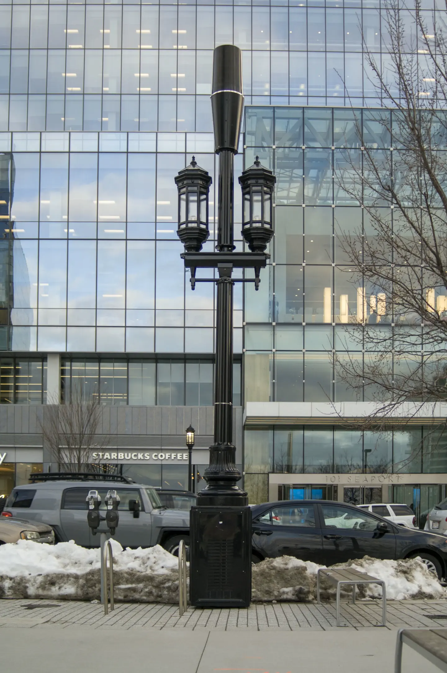 Black ornamental small cell pole with lanterns and a conical antenna shroud in front of a glass office tower